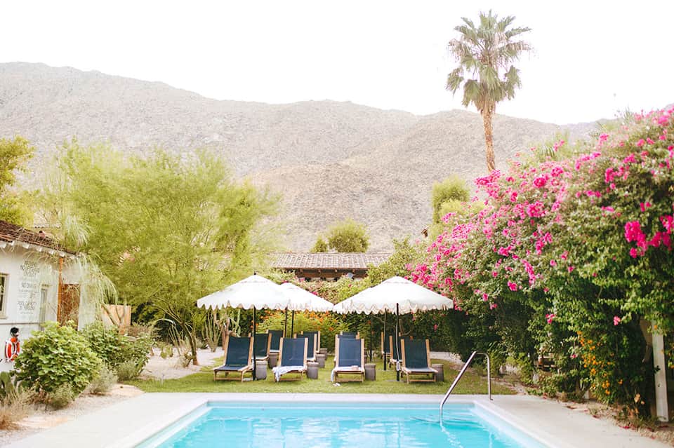 Desert resort pool surrounded by mountains, vibrant pink bougainvillea, and white umbrellas