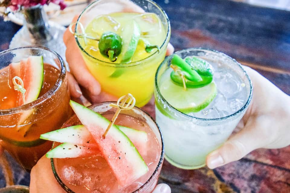 Tropical cocktails with fresh fruit garnishes held by hands at poolside