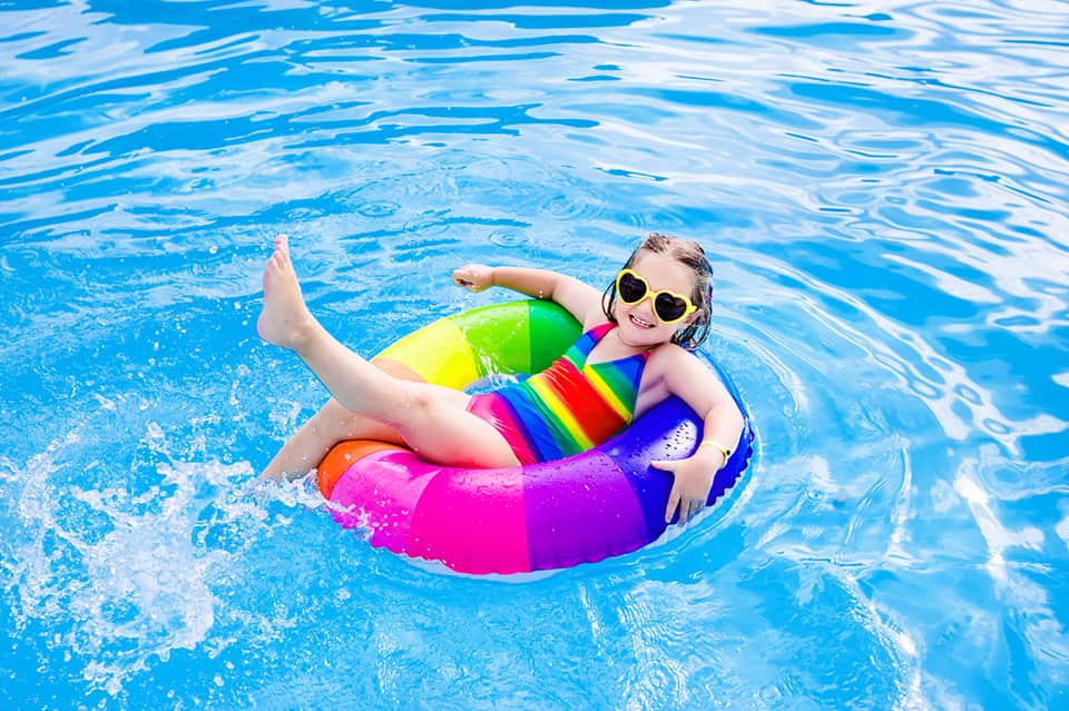 Child in colorful rainbow pool float enjoying bright blue swimming pool water