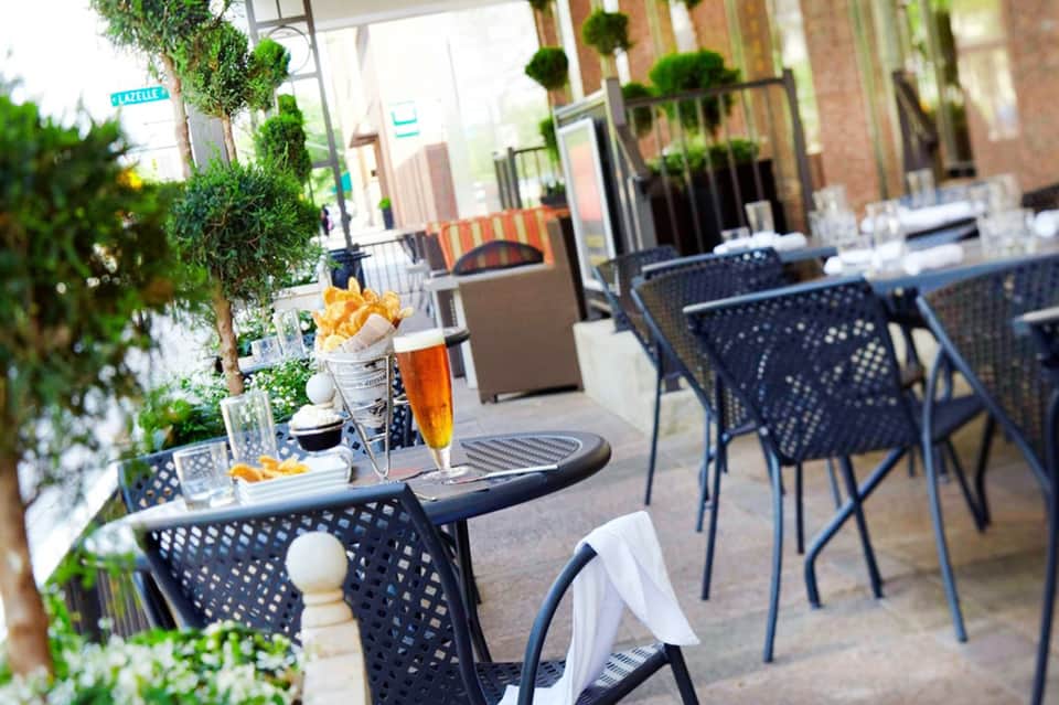 Outdoor dining patio with black mesh chairs, small tables, green ivy walls, and French fries appetizer