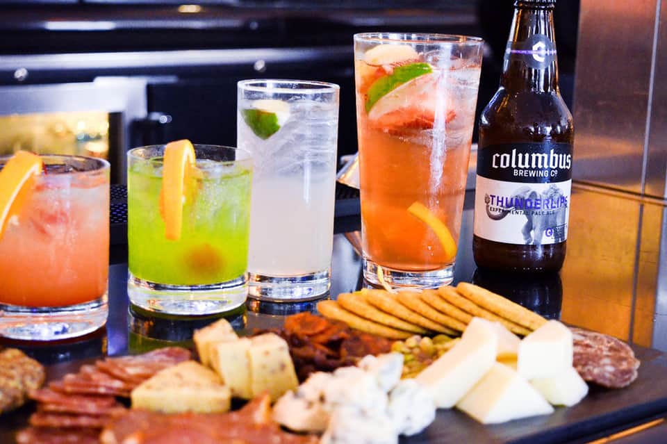 Colorful cocktails and craft beer with charcuterie board on dark counter