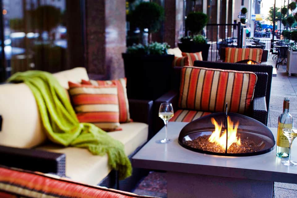 Upscale outdoor fireplace lounge with striped seating, wine glasses, and evening ambiance