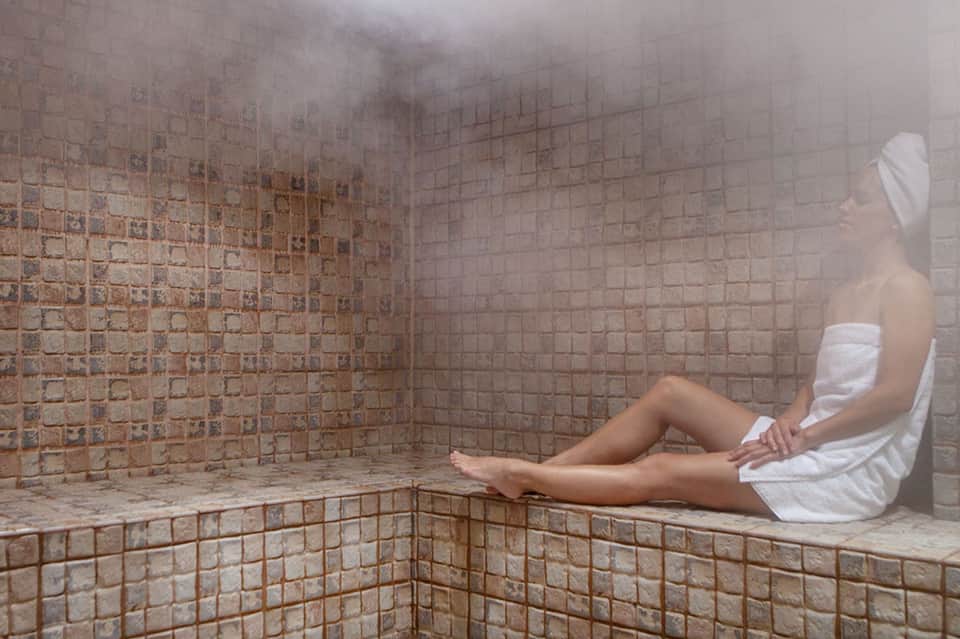 Woman relaxing in a steamy spa room with terracotta tile walls and heated bench seating