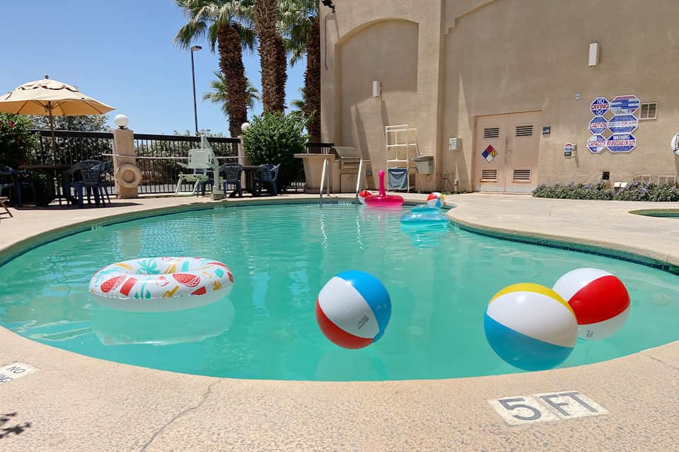 Bright turquoise pool with colorful beach balls and inflatables, palm trees in background