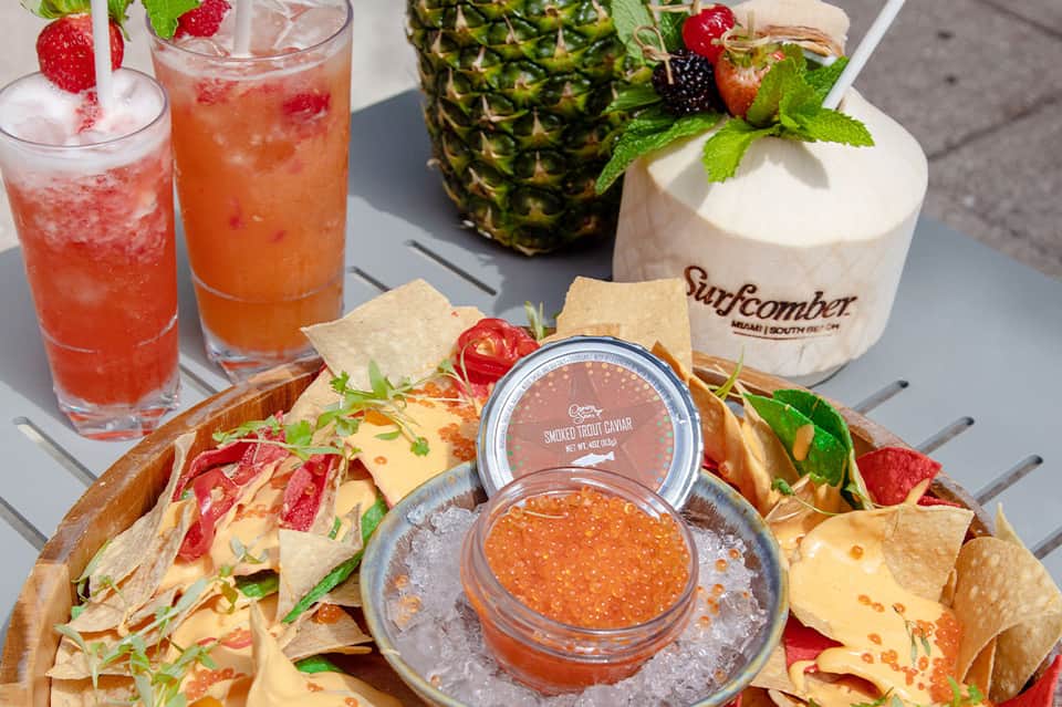 Resort dining spread featuring caviar, fresh pineapple, tacos, and colorful tropical cocktails on outdoor table