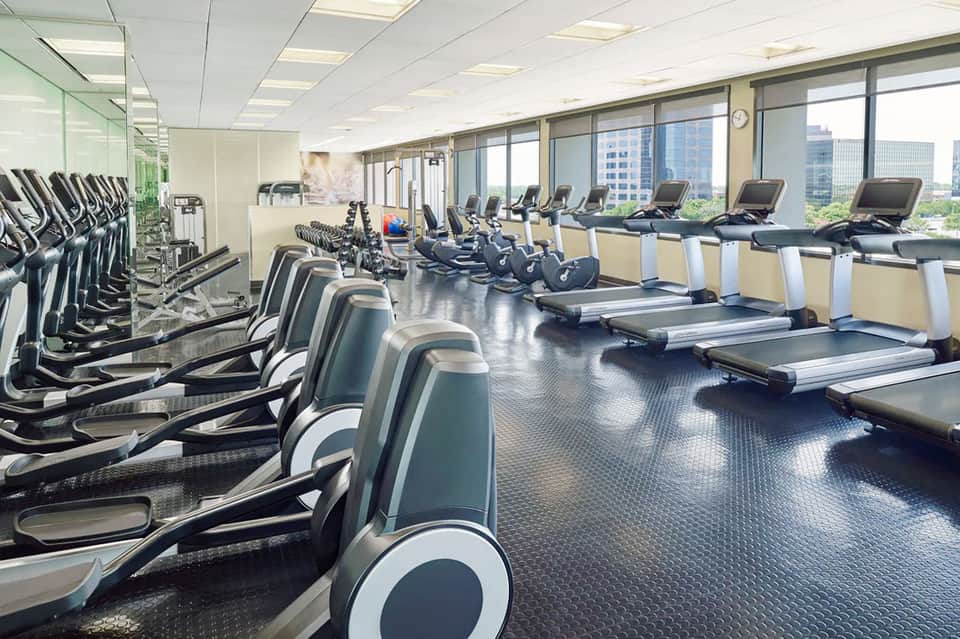 High-rise fitness center with rows of treadmills and exercise bikes facing floor-to-ceiling windows