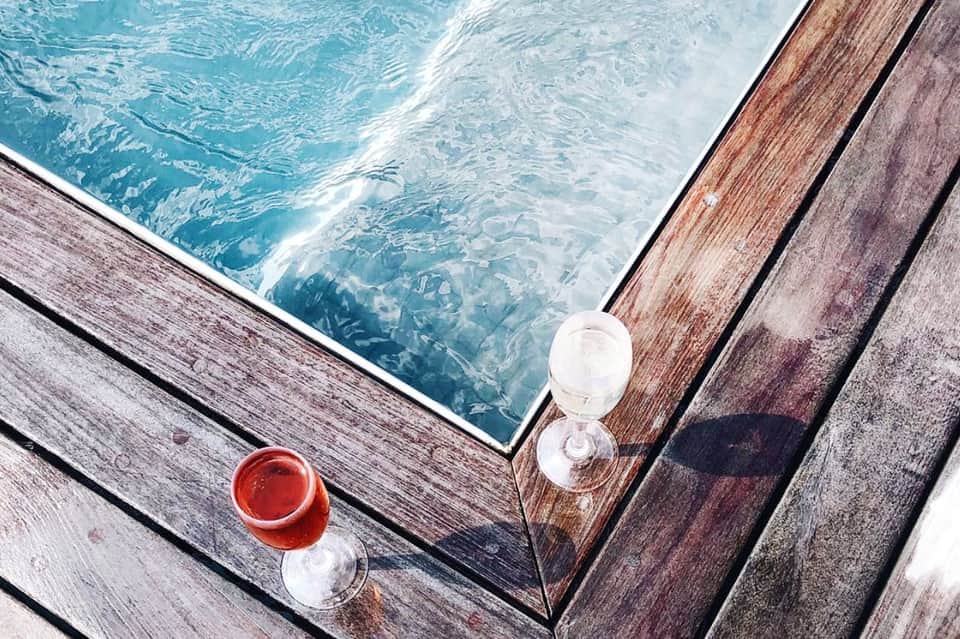 Overhead view of red cocktail and water glass on wooden deck beside turquoise pool