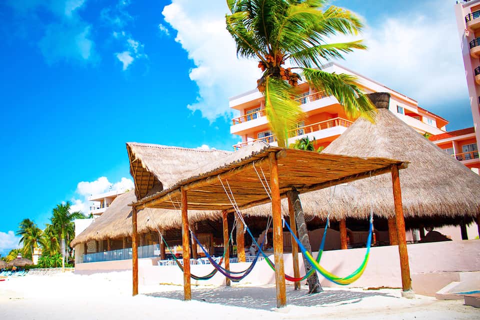 Beachfront resort pool with hammocks, thatched structures, and tropical palms