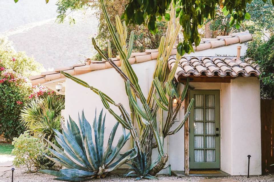 White stucco cottage with terracotta roof and blue agave plants in landscaped garden