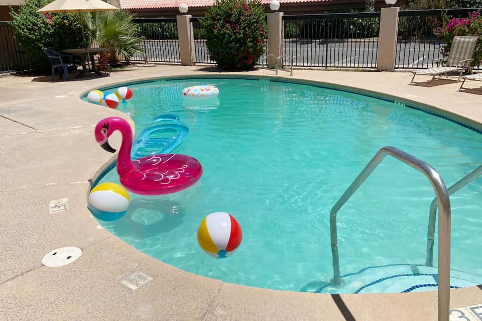Resort pool with colorful floats, lounge chairs, and white umbrellas by building