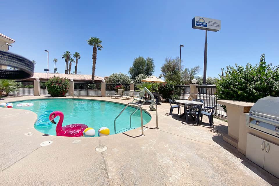 Poolside area with colorful inflatable flamingo float, palm trees, and outdoor seating