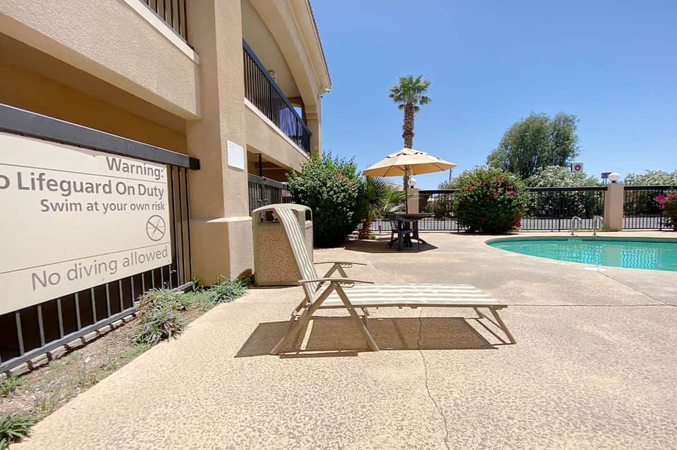 Resort pool area with lounge chairs, yellow umbrella, palm tree, and lifeguard warning sign on sunny day