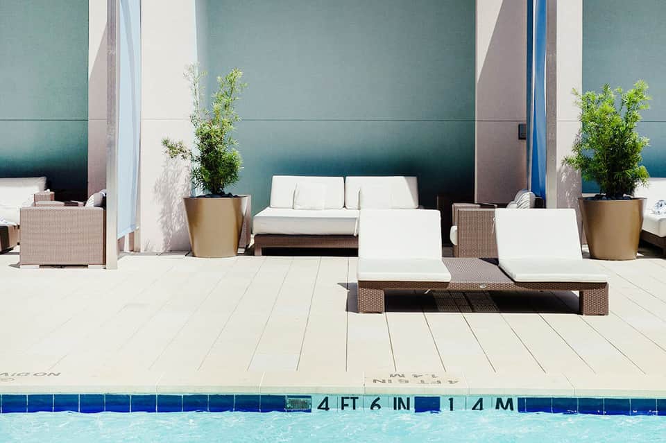 Minimalist pool deck with modern lounge chairs, potted plants, and teal accent wall