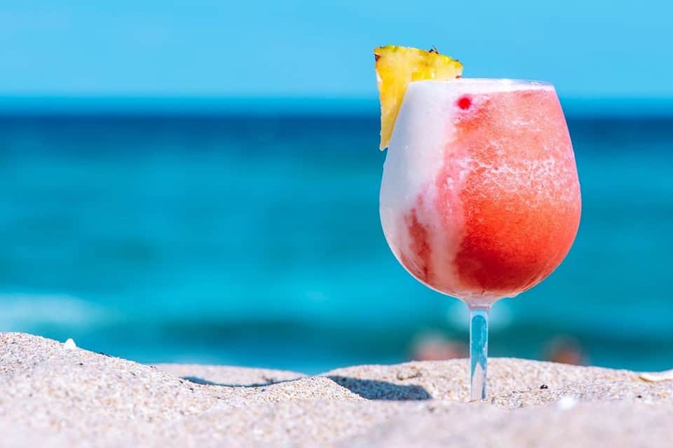 Tropical cocktail with pineapple garnish on sandy beach with ocean backdrop