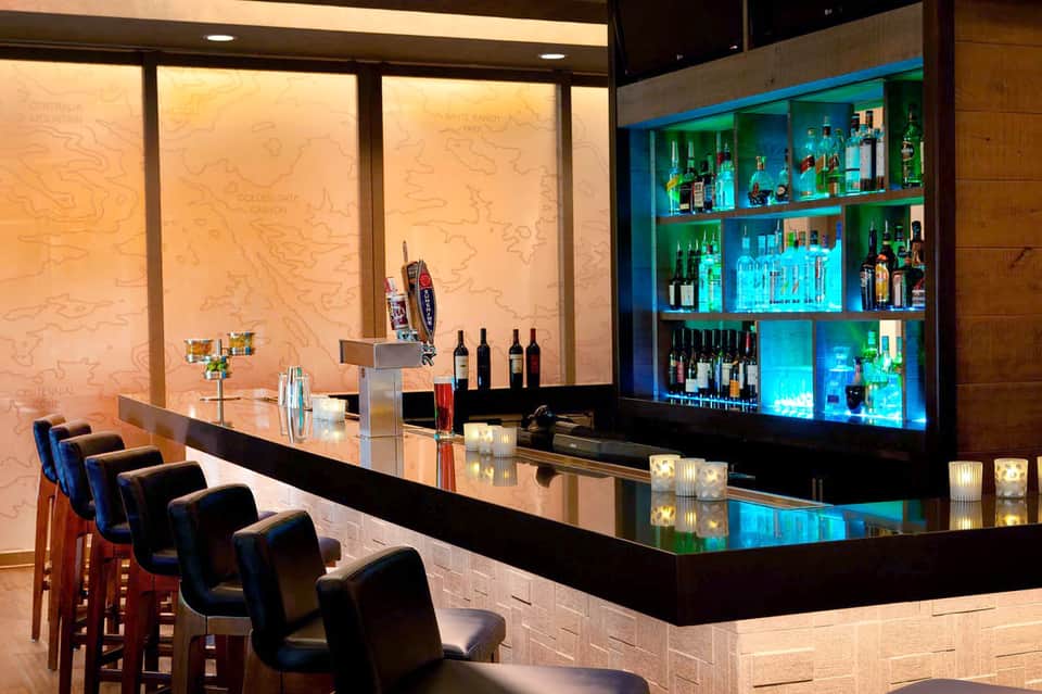 Elegant bar counter with black marble top, illuminated bottle display, and modern seating