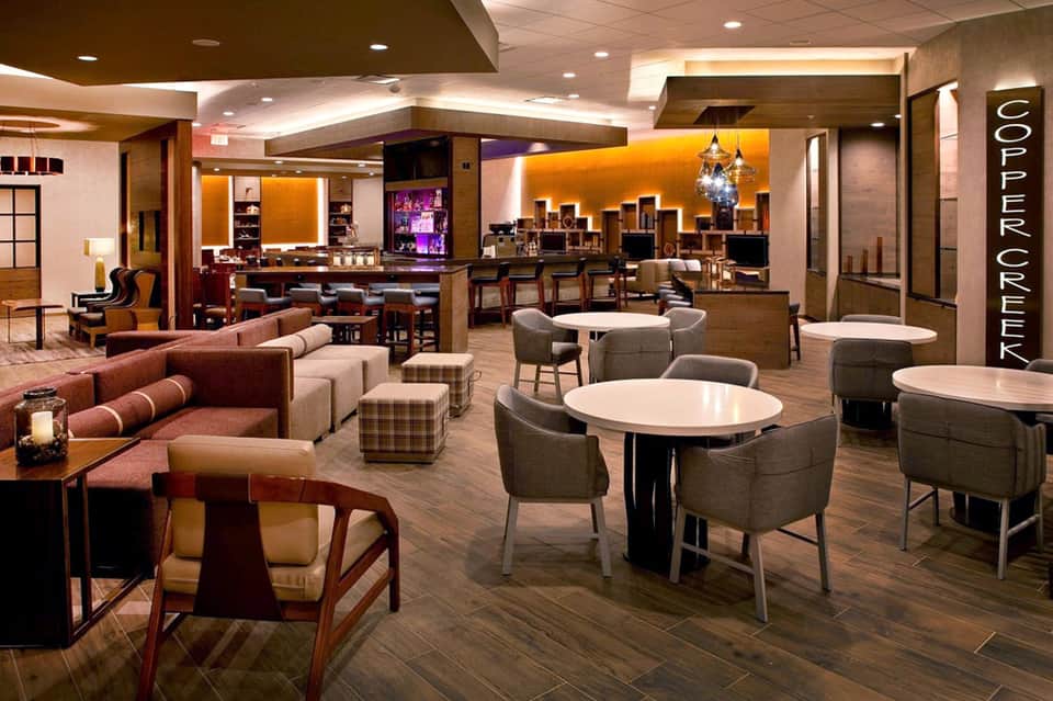 Upscale lounge with warm wood tones, orange accent lighting, bar counter, and seating areas