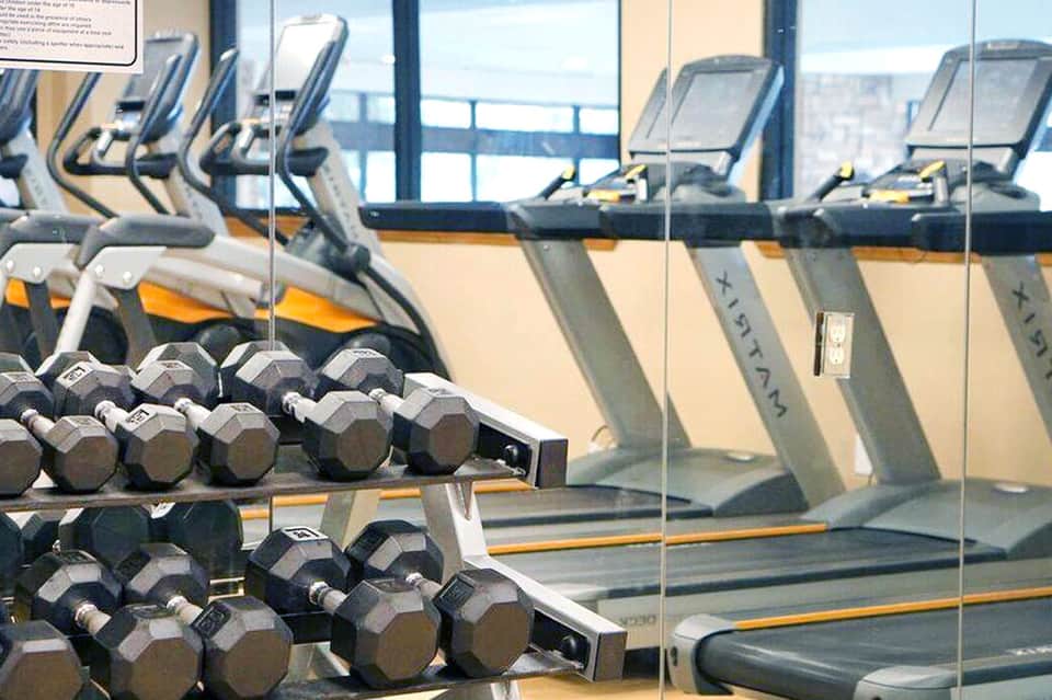 Fitness center with dumbbells in foreground, cardio equipment, and ocean view through windows