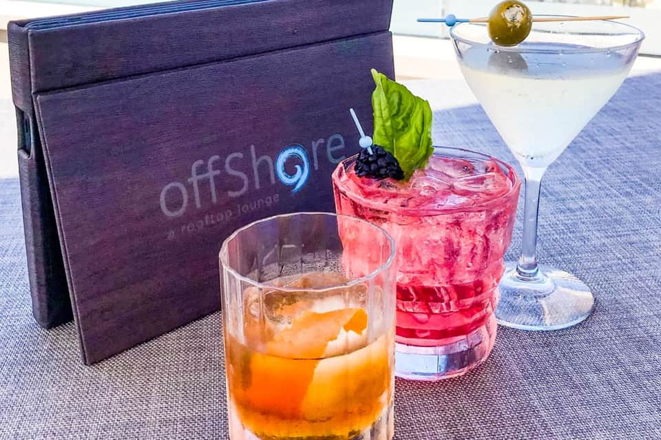 Offshore lounge cocktail menu with three colorful drinks and purple branded menu card on table