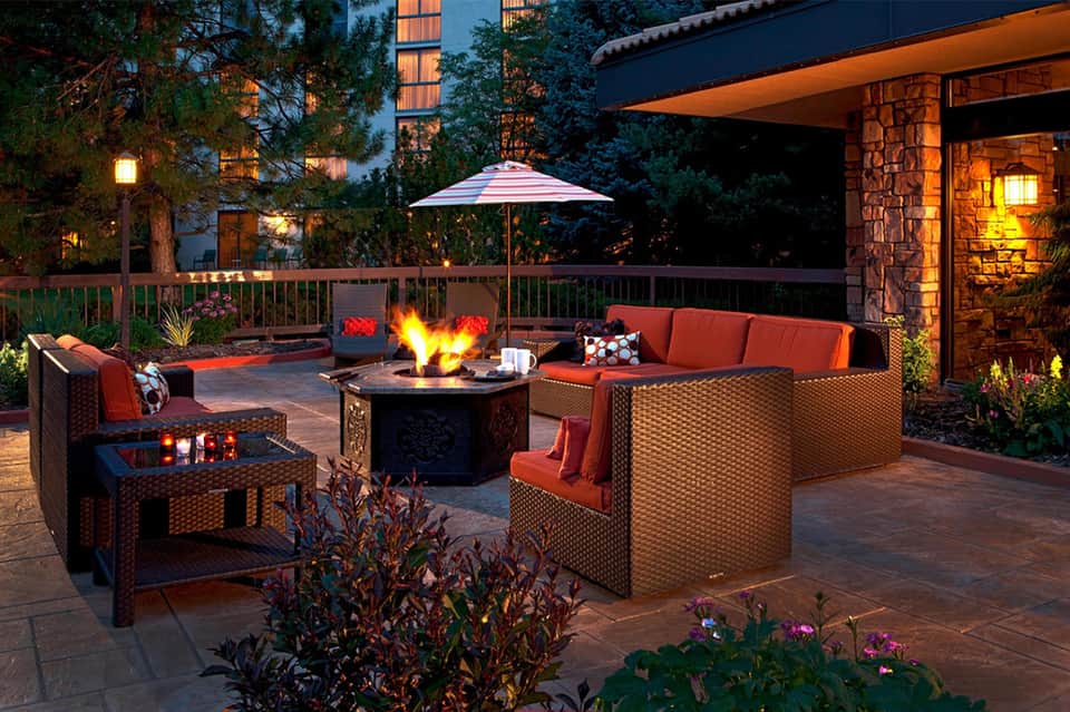 Evening patio seating with fire pit, orange cushioned furniture, lit umbrella, and ambient lighting
