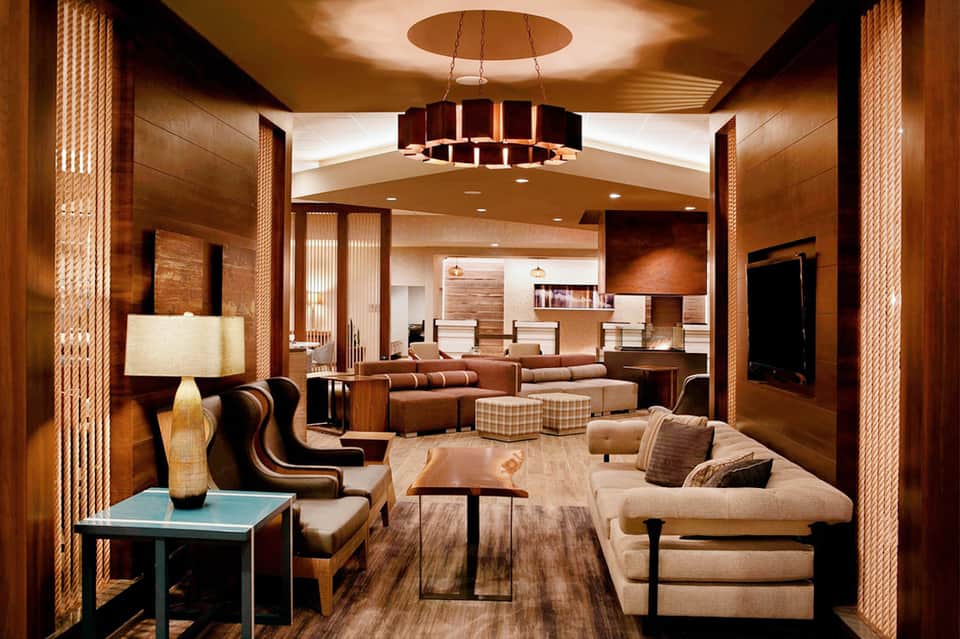 Upscale hotel lobby with wood paneling, modern furniture, and contemporary lighting fixtures