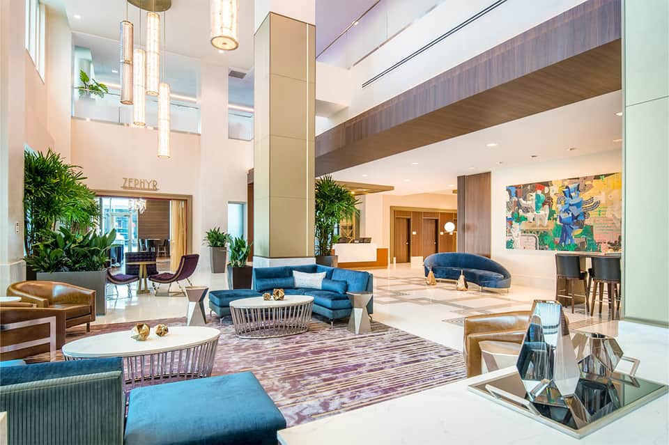 Modern hotel lobby with high ceilings, blue seating, pendant lighting, and contemporary art
