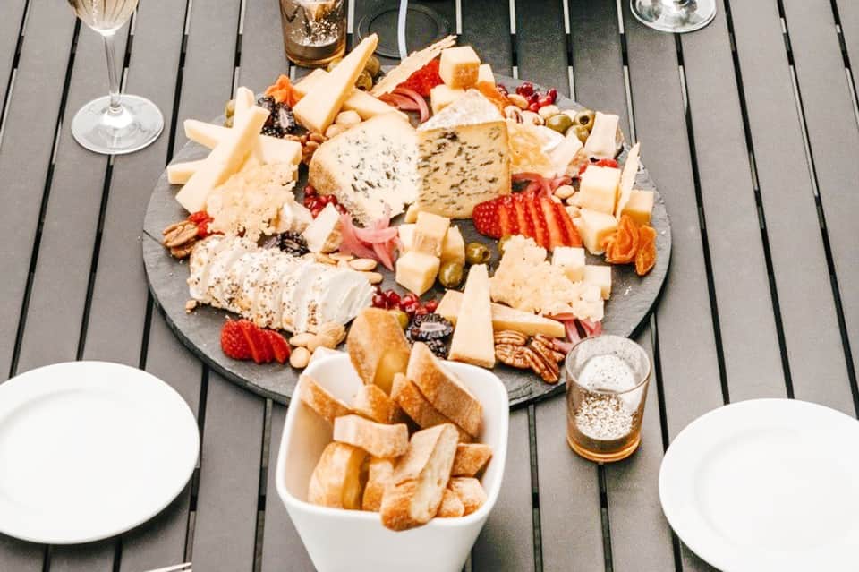 Gourmet charcuterie board with assorted cheeses, cured meats, nuts, and fruits on gray deck