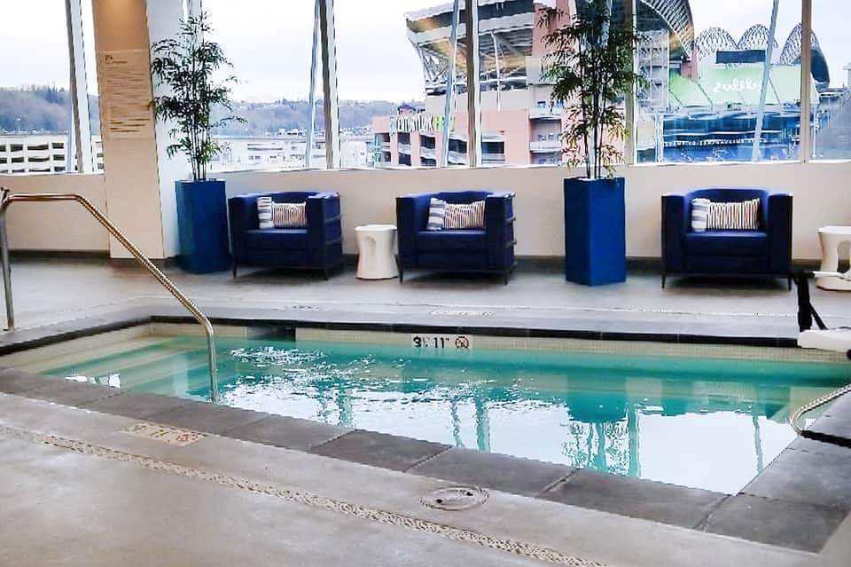 Indoor pool area with blue armchairs, large windows overlooking city skyline and waterfront