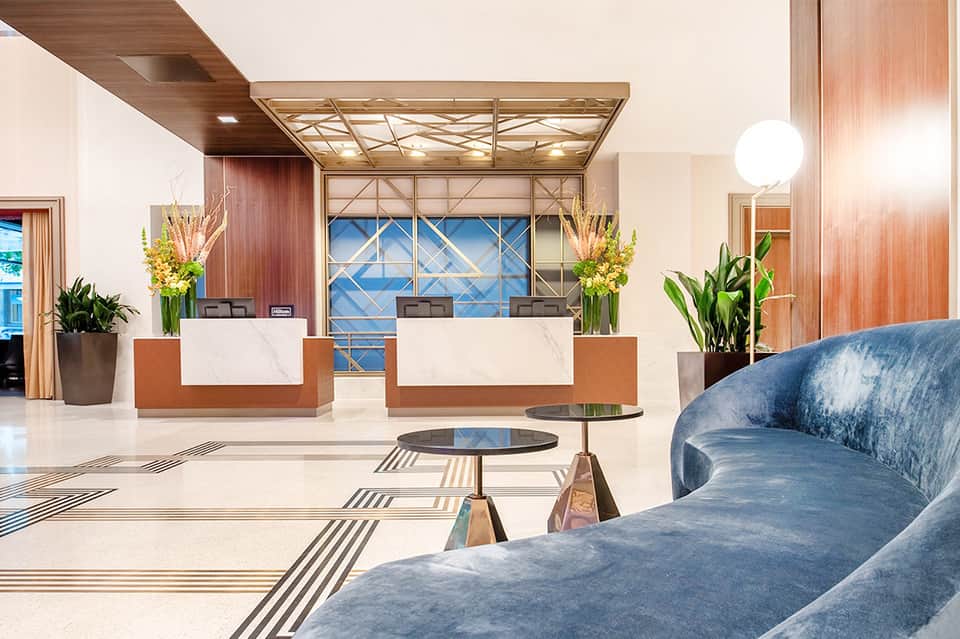 Contemporary hotel lobby with dual reception desks, marble floors, and geometric window design