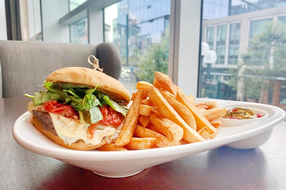 Upscale cheeseburger with crispy fries served on white plate with city view behind