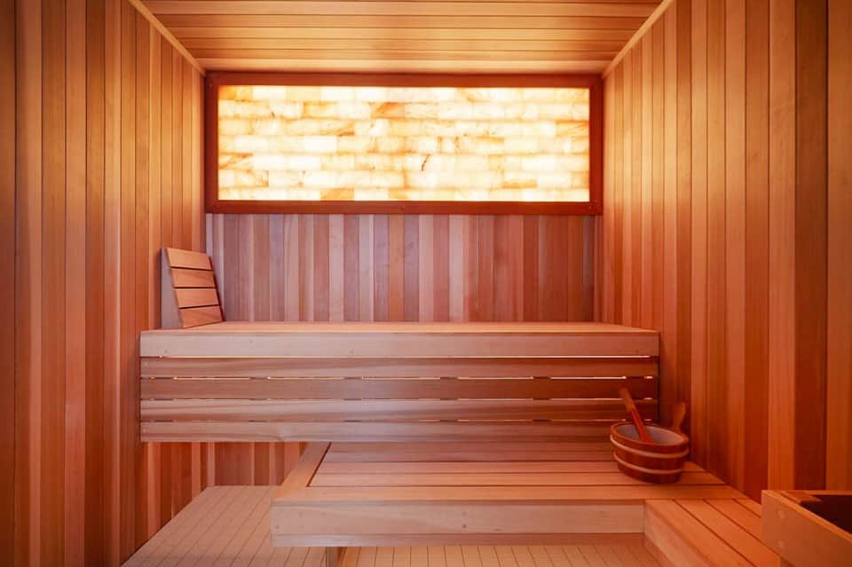 Wooden sauna interior with stone window, bench seating, and traditional hot stone accessories