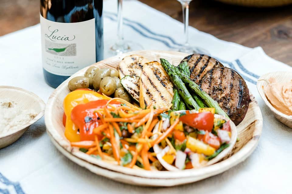 Grilled steak, asparagus, potatoes, and colorful vegetable salad with wine bottle on white plate