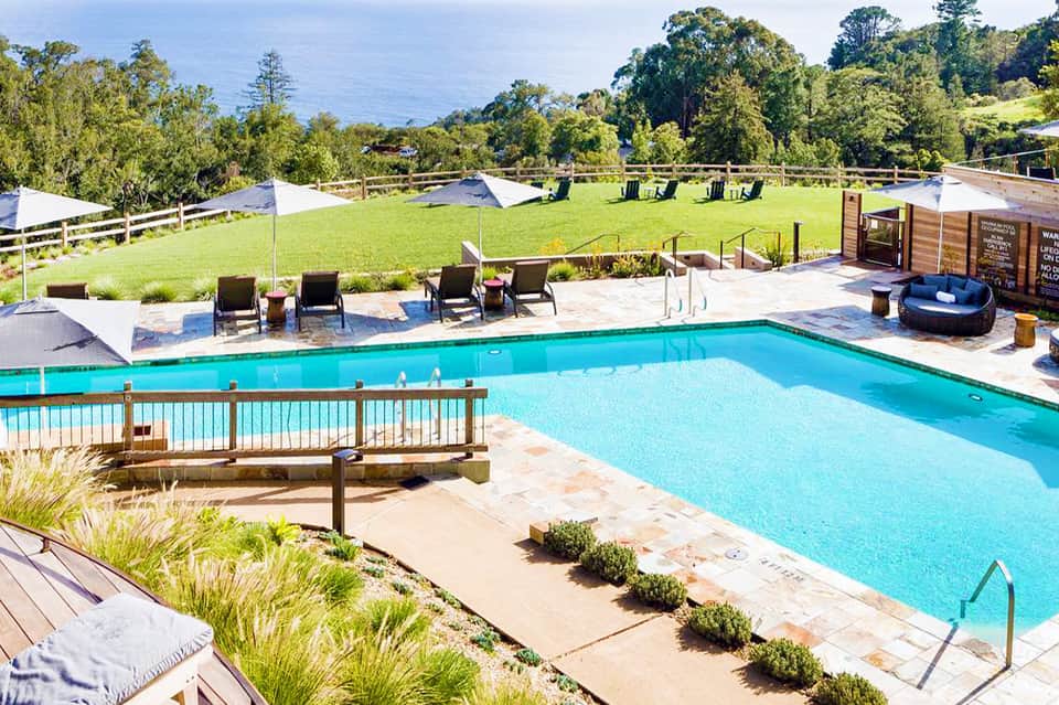 Resort pool with turquoise water, lounge chairs, and grassy grounds with ocean view