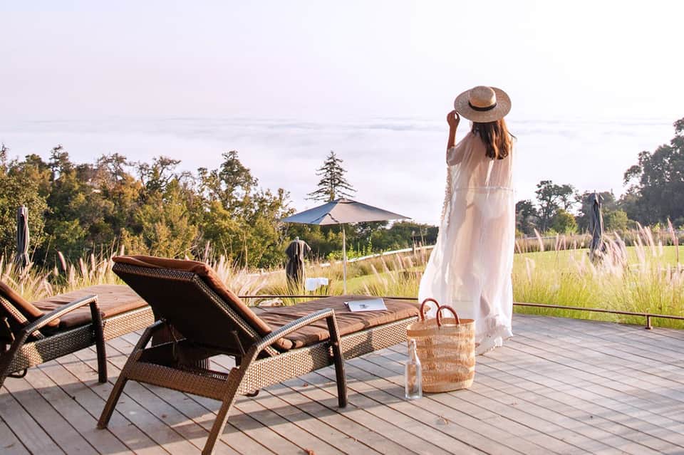 Woman in white dress standing on wooden deck overlooking peaceful lake and wetland landscape