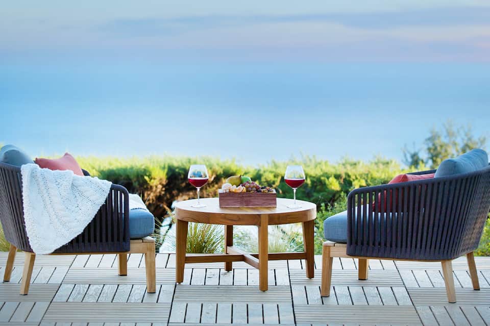 Two lounge chairs facing a wetland landscape with wine glasses and blanket on a wooden deck