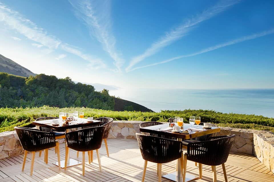 Clifftop oceanview dining tables with black chairs, ocean horizon, and coastal vegetation