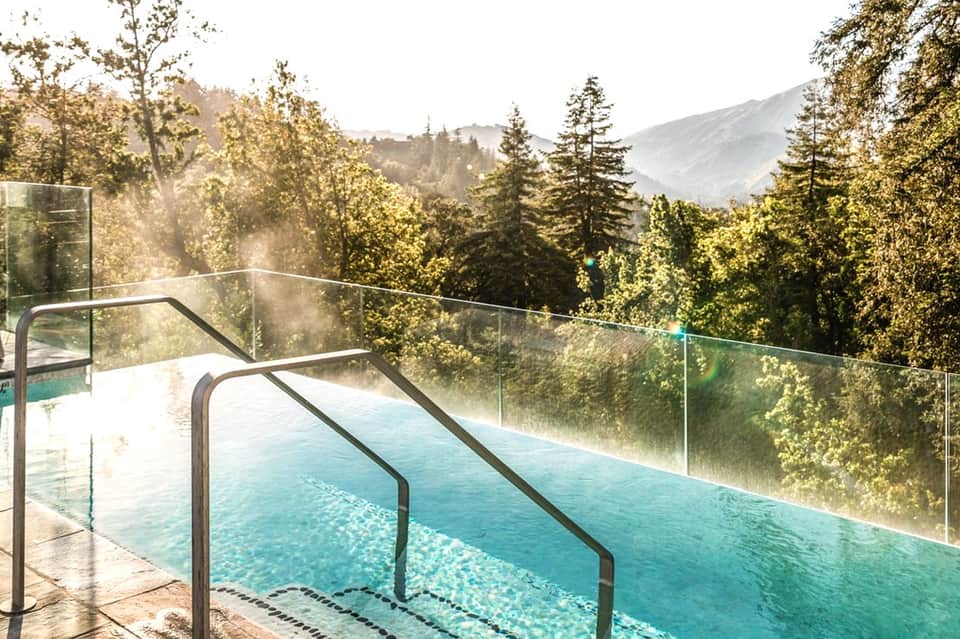 Infinity pool overlooking forested mountains with glass railings and lounge chairs
