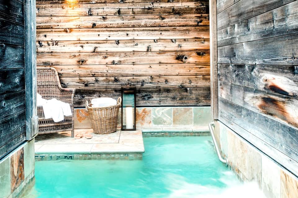 Rustic wooden spa interior with turquoise mineral pool and wicker seating area