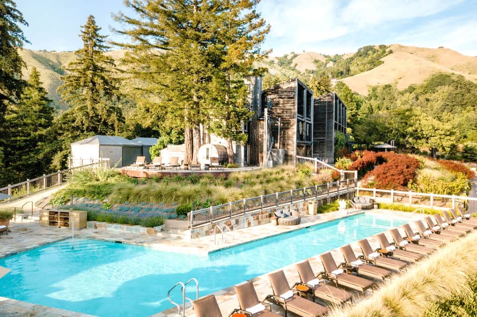 Luxury spa resort with heated pool, lounge chairs, mountains, modern wood structures, and lush grounds