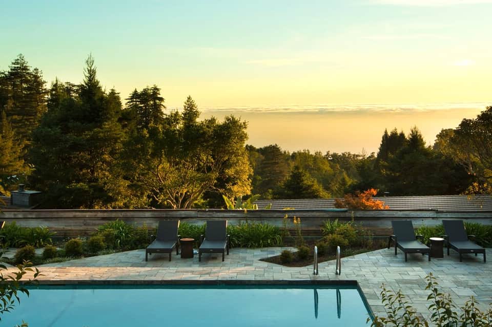 Modern pool overlooking serene lake at sunset with lounge chairs and landscaping