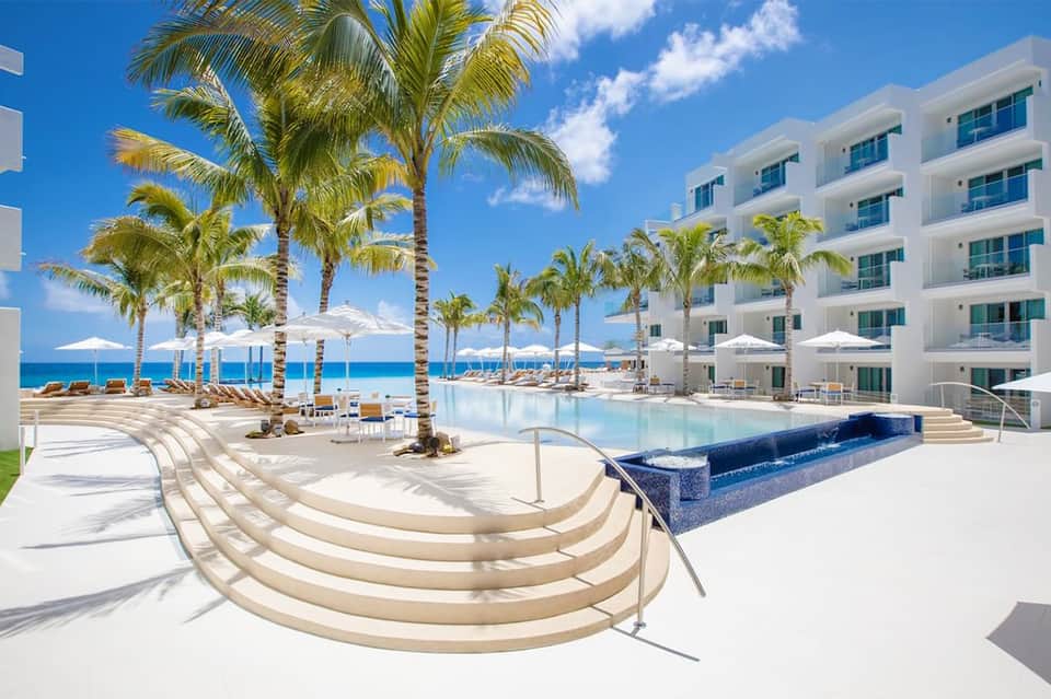 Beachfront resort with curved pool, palm trees, white building facade, and ocean views under blue sky