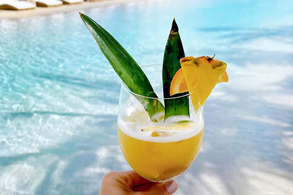 Tropical cocktail with pineapple garnish held against turquoise ocean and sky