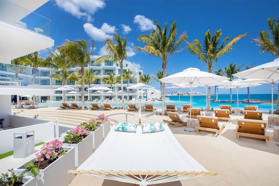 Beachfront resort deck with white umbrellas, lounge chairs, and turquoise water
