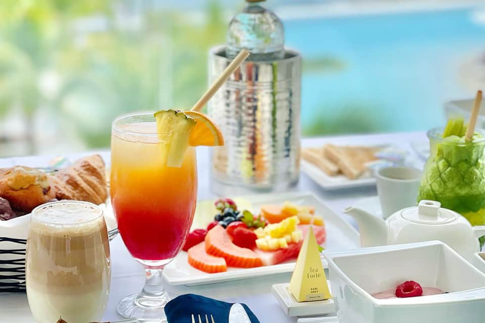 Tropical poolside dining with colorful cocktail, fresh fruit, and ocean backdrop