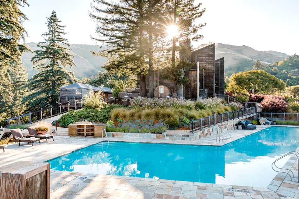 Resort pool surrounded by mountains, with modern architecture, loungers, and landscaped gardens under blue sky