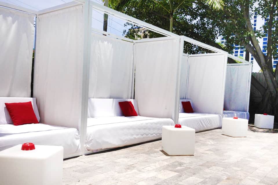 Modern white cabana beds with red pillows and privacy curtains in resort courtyard setting