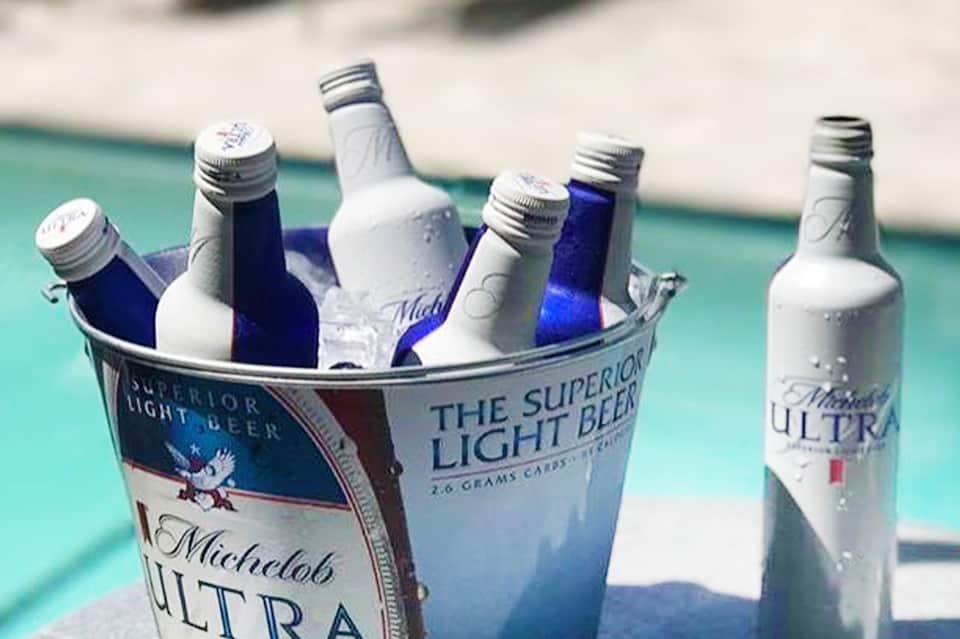 Ice bucket with cold beer bottles and condensation by resort pool with turquoise water in background