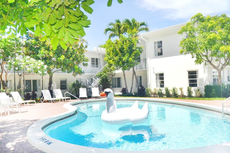 Resort courtyard with white buildings, pool, lounge chairs, and palm trees