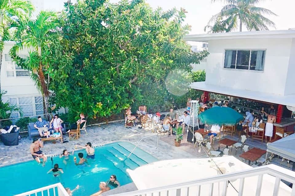 Aerial view of resort courtyard with swimming pool, palm trees, and guests at beachfront property