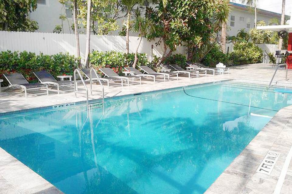 Rectangular pool surrounded by lounge chairs and palm trees in tropical courtyard
