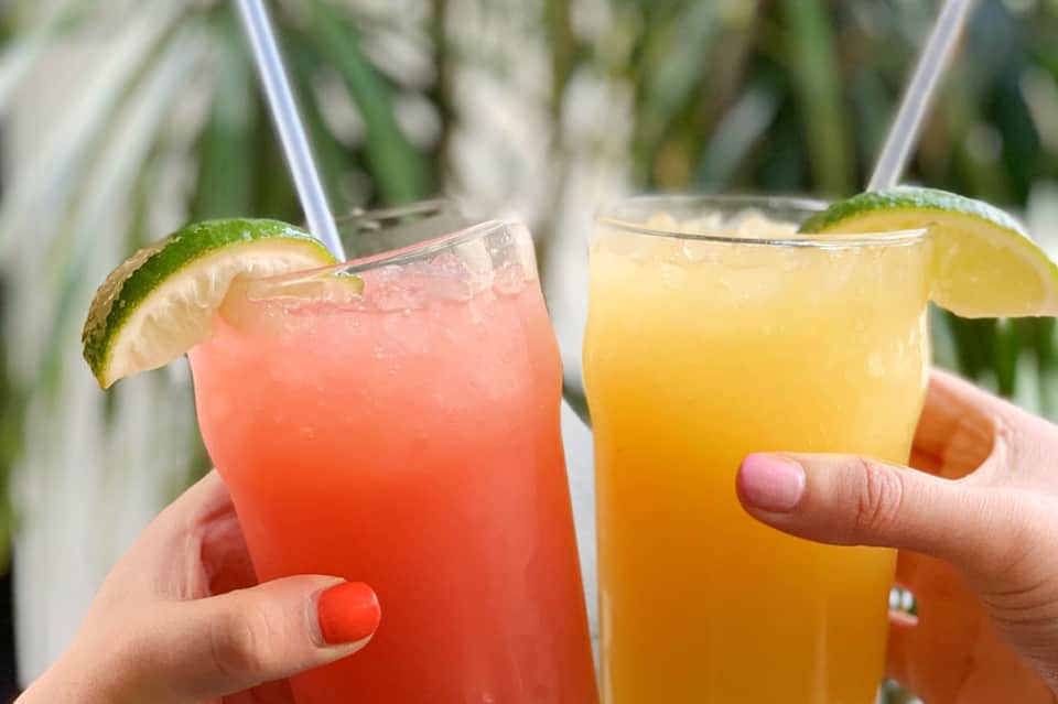 Two colorful cocktails with lime garnish held in hands at tropical venue